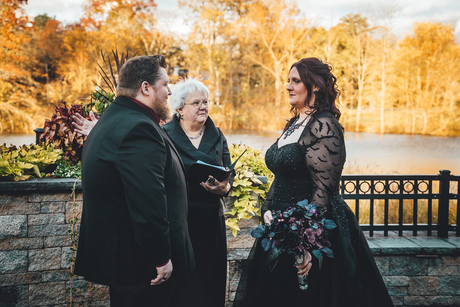 Wedding ceremony at The Pond House with fall foliage and pond backdrop